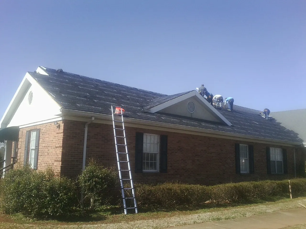 Crew tearing shingles off a brick ranch roof with a ladder set — Emergency Roof Repair work by our crew in Tabor