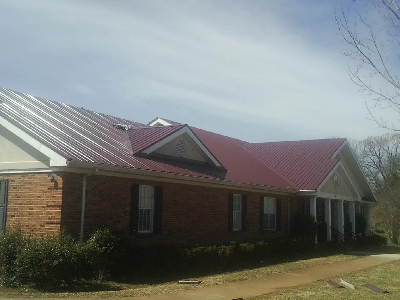 Red metal roof with gabled entries on a long brick building, from a Hail Damage Roof Repair job in Tabor