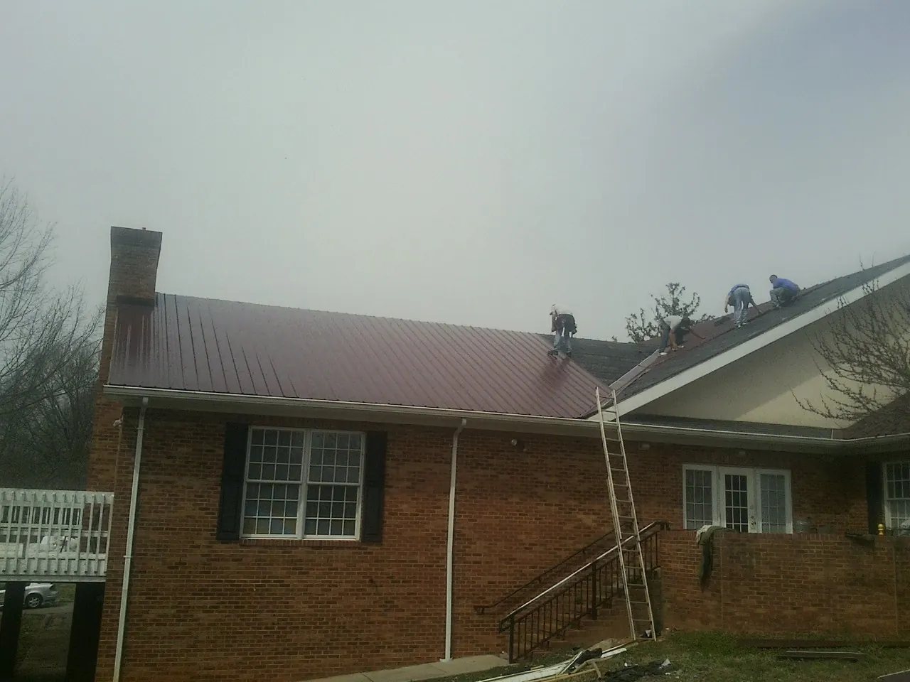 Crew setting red metal roofing panels on a brick home in Tabor