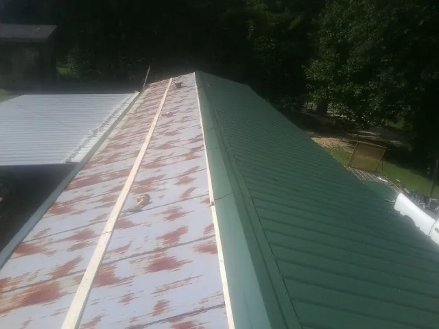 Old rusted panels beside newly installed green metal roofing — Wind Damage Roof Repair by Roofing Brothers in Tabor