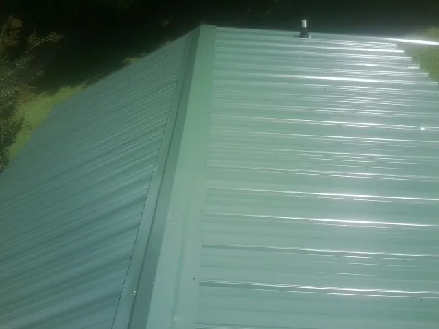 New green metal panels meeting at the ridge of a roof — Flat Roof Repair work by our crew in Tabor