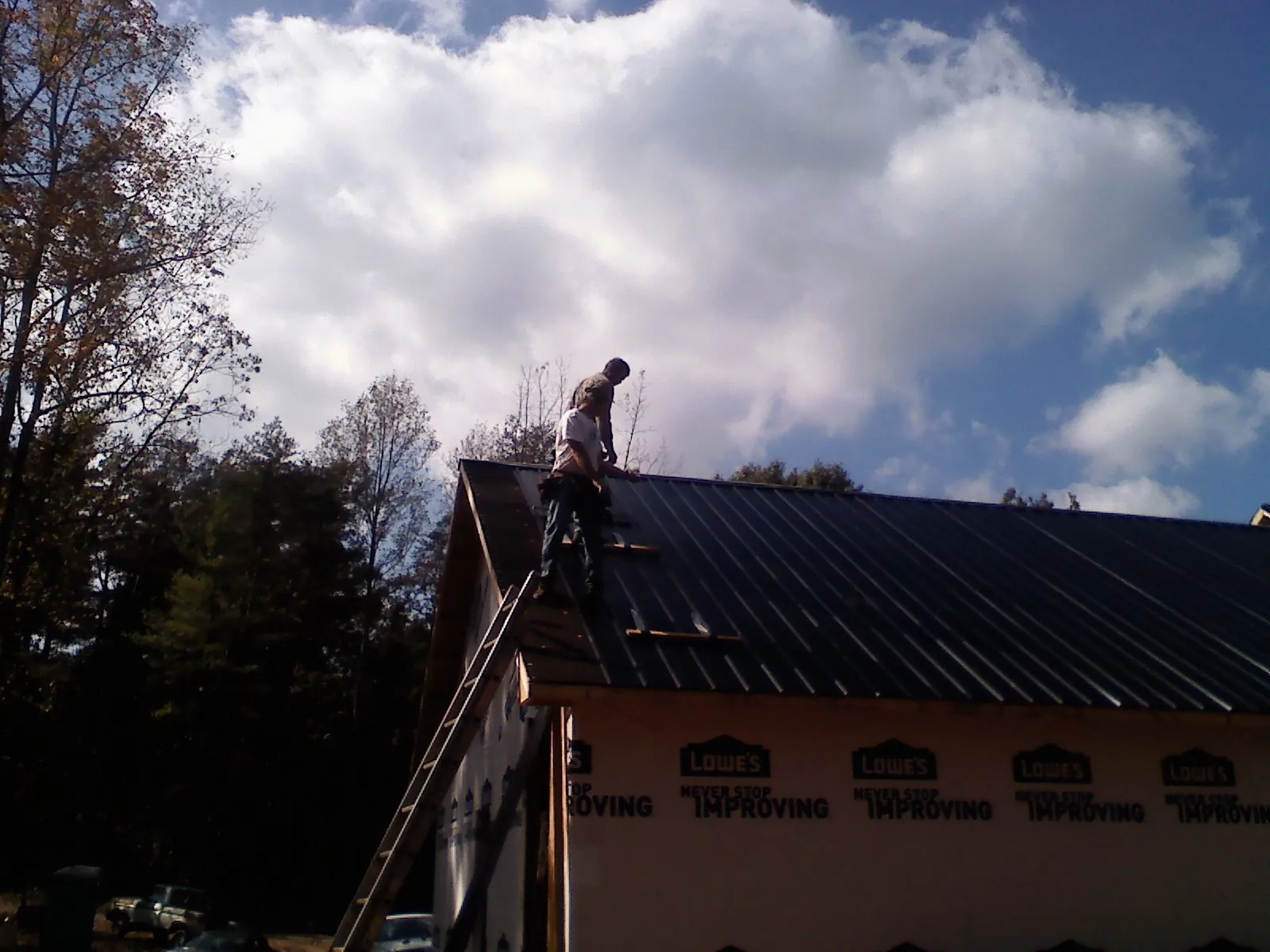 Roofer fastening dark metal panels high against a cloudy sky, from a Roof Inspection job in Tabor