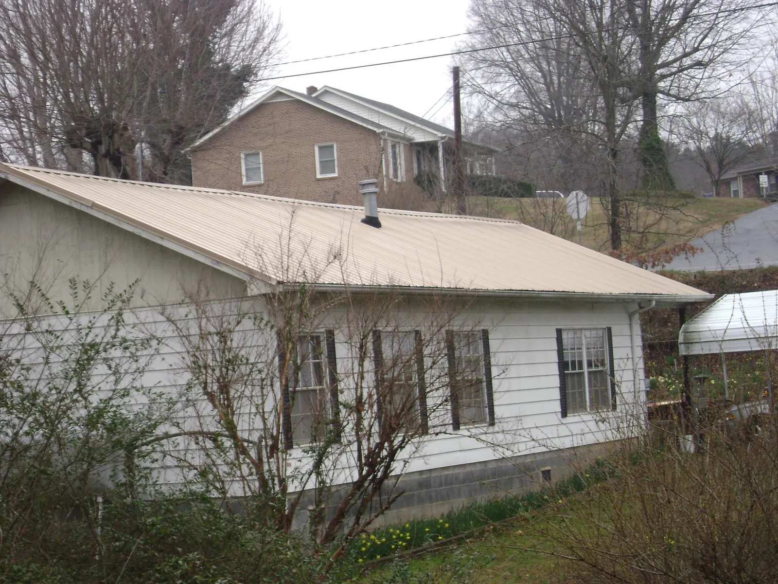 Tan metal roof on a white sided house set into a hillside — Commercial Roofing by Roofing Brothers in Tabor