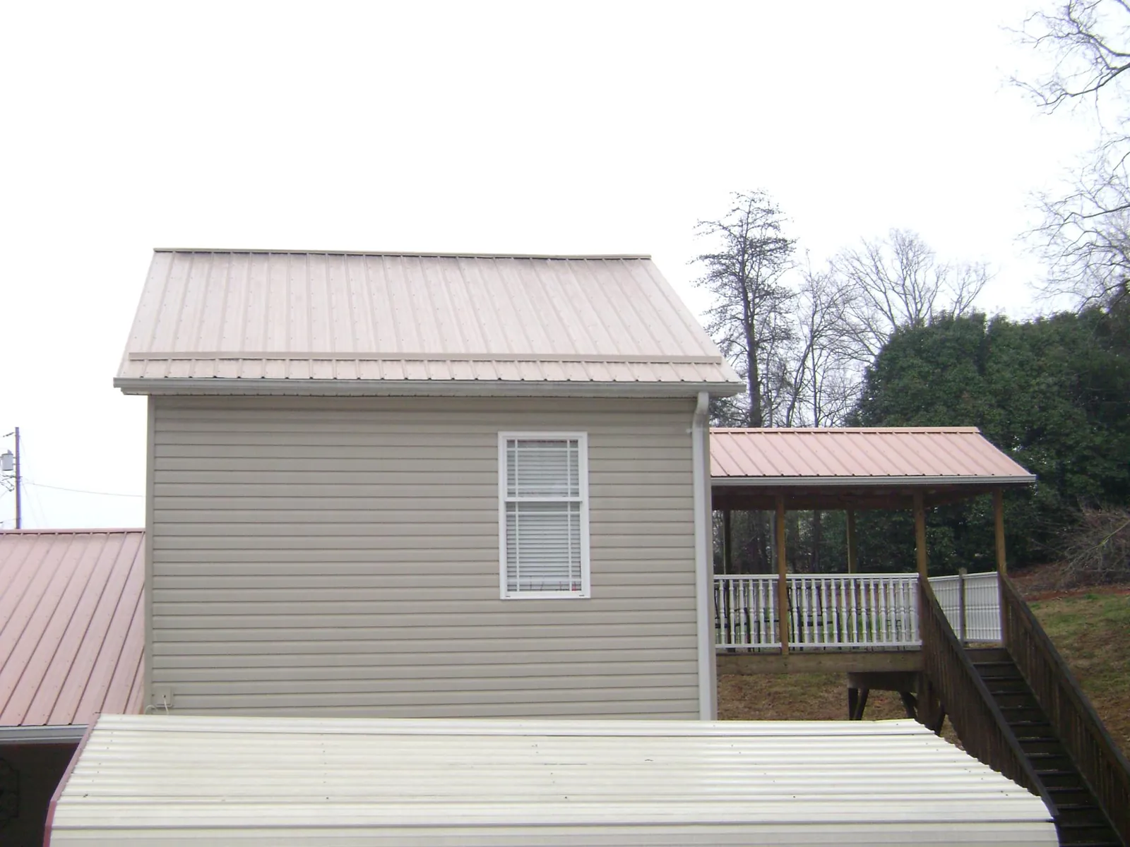 Tan metal roofs on a two story addition and attached porch, from a Roof Replacement job in Tabor